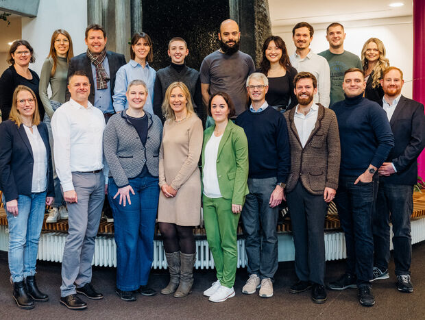 Eine Gruppe von 18 Personen, die in einem Haus zusammen stehen und für ein Foto posieren.