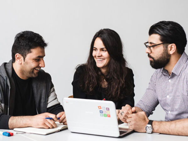 Drei junge Erwachsene sitzen am Tisch mit Laptop und besprechen sich.