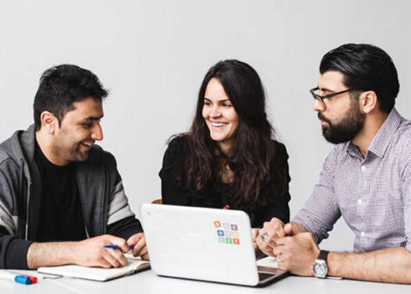 Drei junge Erwachsene sitzen am Tisch mit Laptop und besprechen sich.