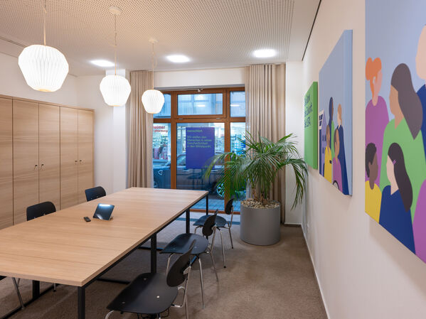 Moderner Konferenzraum mit einem langen Tisch, Stühlen, Schränken und Wandbildern.