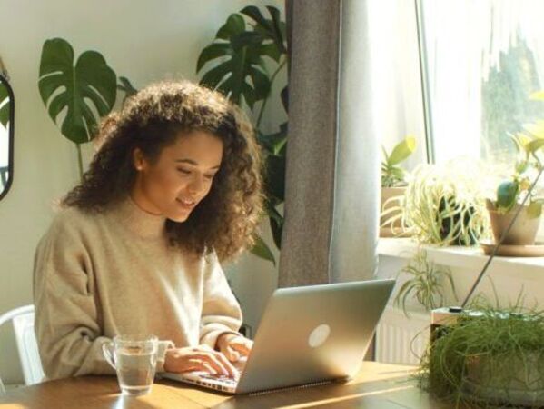 Frau sitzt mit Laptop an einem Tisch mit Pflanzen
