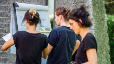 Drei Personen stehen an einem Flipchart mit Notizen in einer Außenumgebung.