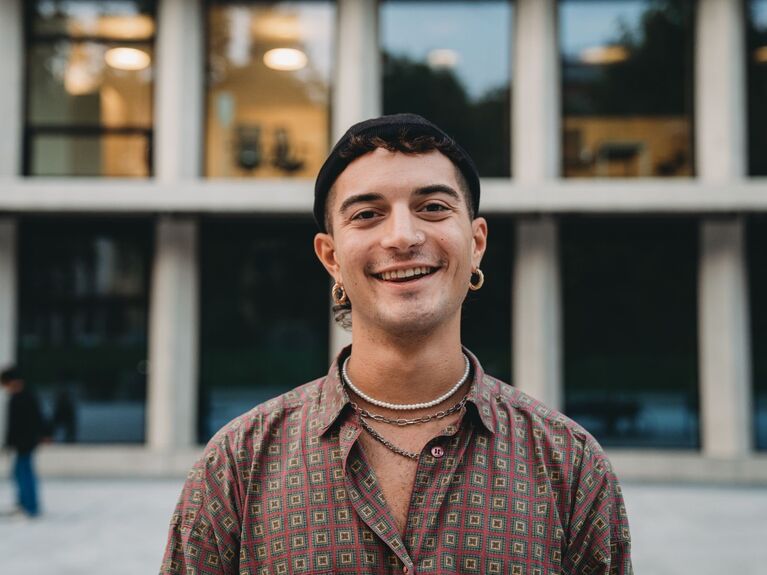 Lächelnde junge männlich gelesene Person mit kurzen dunklen Haaren.