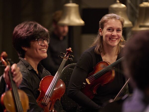 Zwei Geiger sitzen und lächeln während einer Orchesteraufführung.