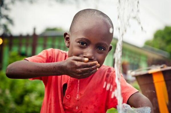 Junge Person of Color schöpft Trinkwasser mit der Hand.