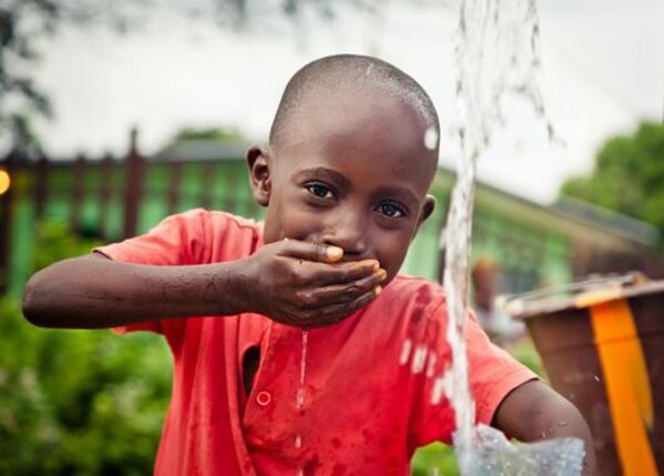 Junge Person of Color schöpft Trinkwasser mit der Hand.