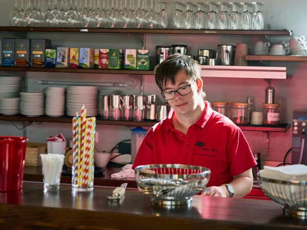 Eine Person in einem roten Hemd arbeitet hinter dem Tresen eines Cafés.