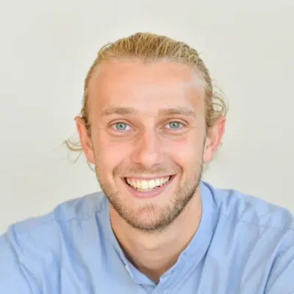 Ein Mann mit blondem Haar und Bart lächelt in die Kamera, er trägt ein hellblaues Hemd.