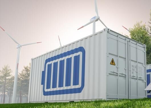 Container mit Batterieaufdruck, im Hintergrund Windkraftanlagen