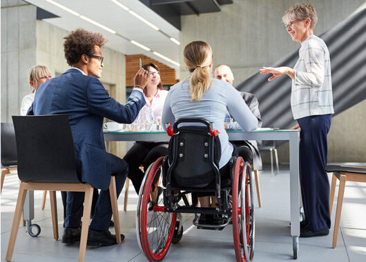 Menschgruppe bei einem Meeting, eine Person im Rollstuhl