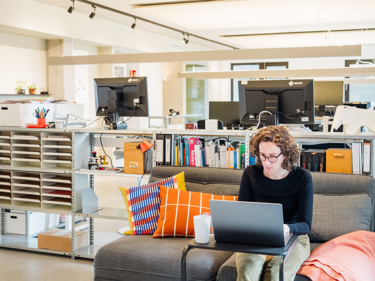 Eine weiblich gelesene Person auf einem Sofa vor einem Laptop