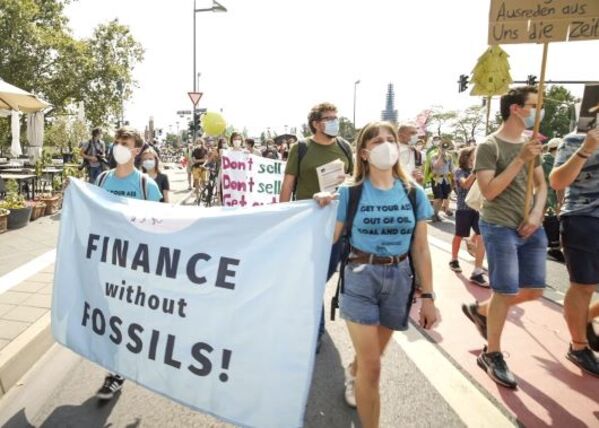 Eine Demonstration mit vielen Menschen und Schildern im Hintergrund. Im Vordergrund tragen 2 Personen ein großes Banner auf dem steht "finance without fossils"