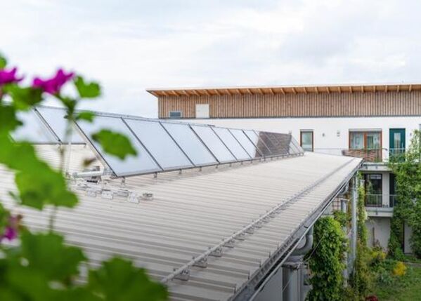 Auf dem Metalldach eines modernen Gebäudes installierte Solarmodule, mit Pflanzen in der Nähe.