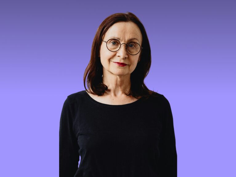 Frau mit Brille in einem schwarzen Hemd vor einem lila Hintergrund mit Farbverlauf.