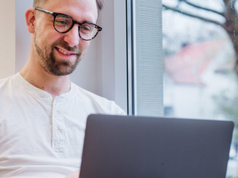 Die GLS Bank berät Unternehmen rund um den Zahlungsverkehr Männlich gelesene Person schaut auf Laptop Monitor