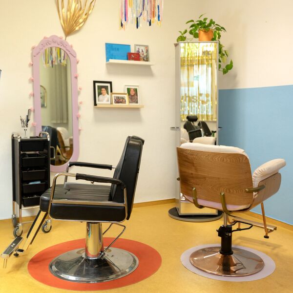 Zwei Friseurstühle stehen in einem dekorierten Salon vor Spiegeln.