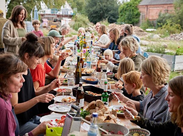 Lange Tafel mit Essen und Trinken an der Bewohnende aus verschiedener Altersgruppen gemeinsam essen.