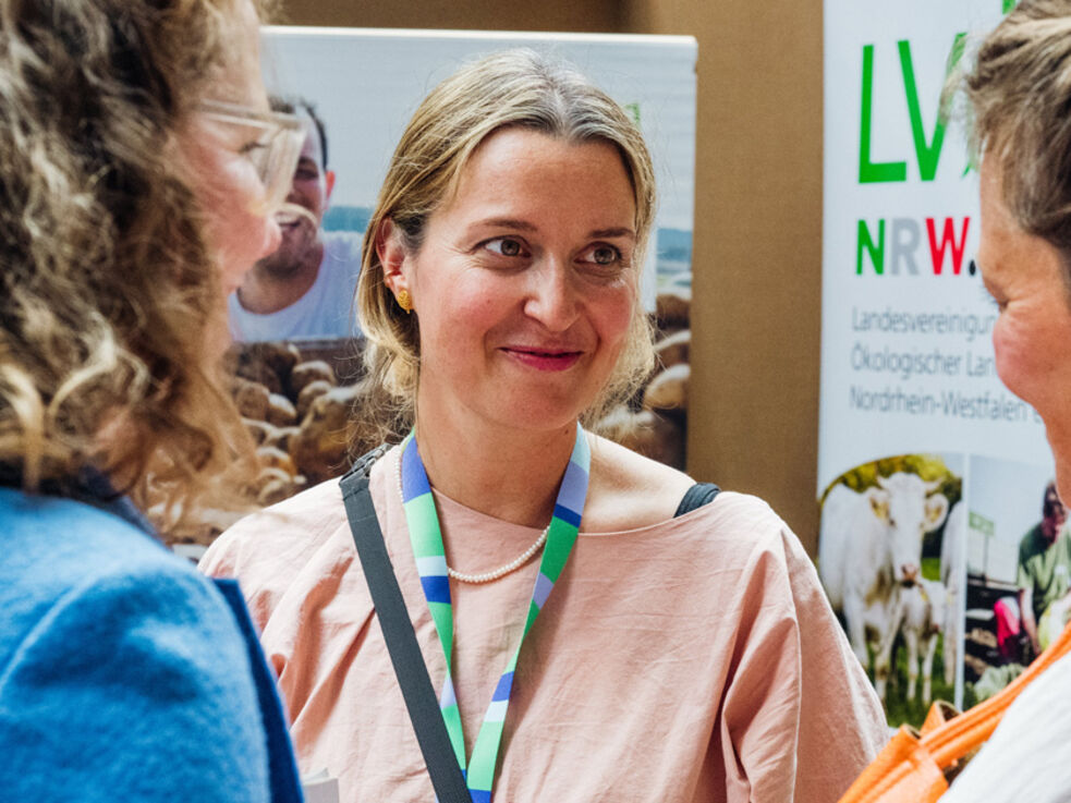 Drei weiblich gelesene Personen auf einer Veranstaltung im freundschaftlichen Gespräch