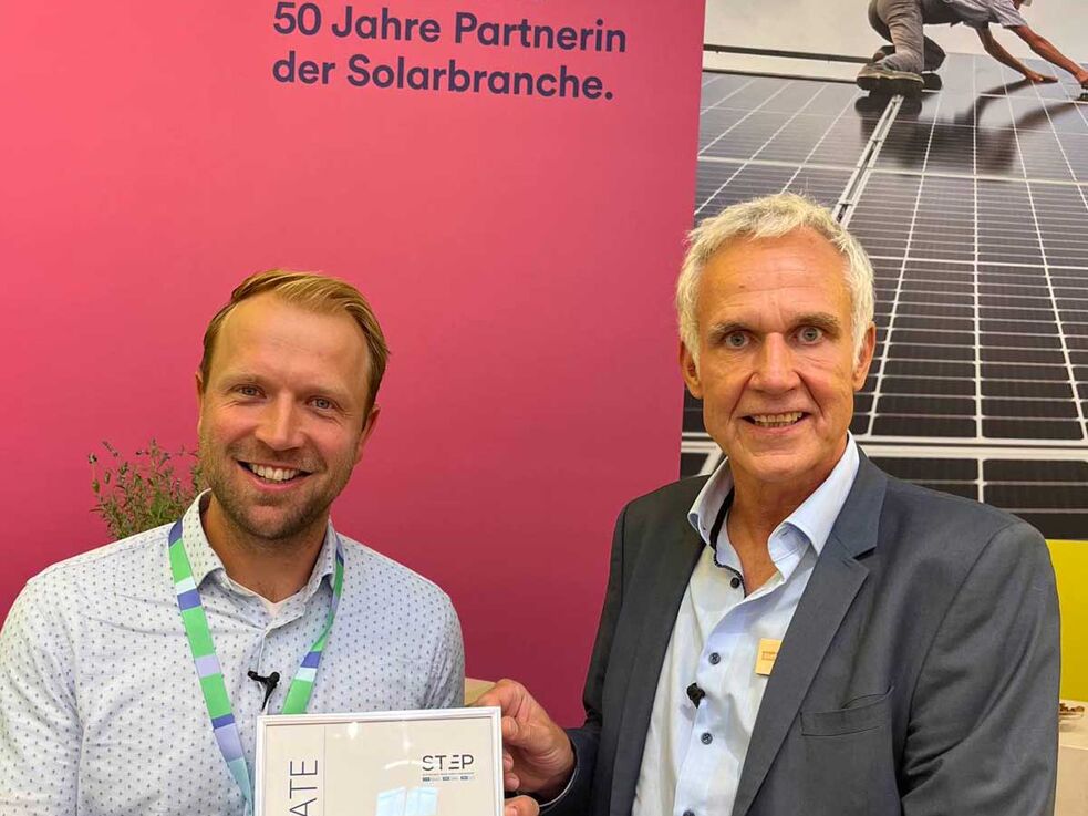 2 männlich gelesen Personen. Michael Orth (links) hält Auszeichnung der Intersolar Messe für den nachhaltigsten Messestand in den Händen
