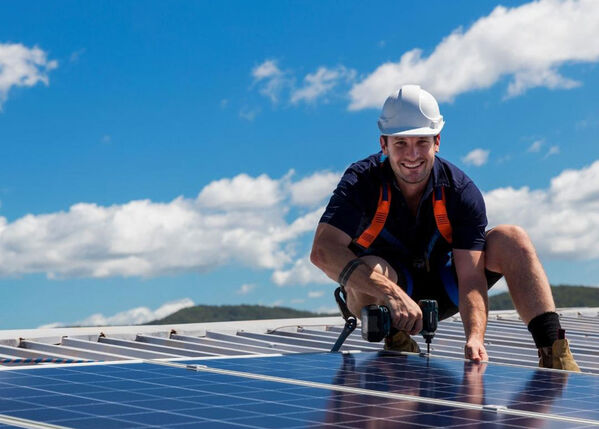 Männlich gelesene Person arbeitet auf einem Dach mit Photovoltaik.