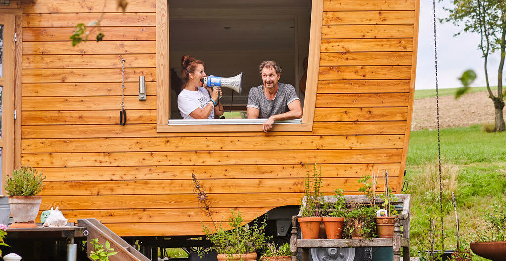 Finanzieren Weiblich gelesene Person spricht im Tiny House männlich gelesene Person mit Megafon an