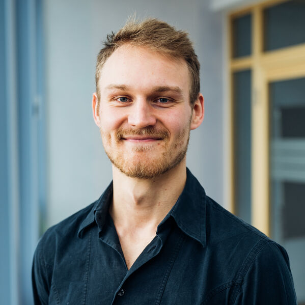 Eine junge männlich gelesene Person mit blonden kurzen Haaren.