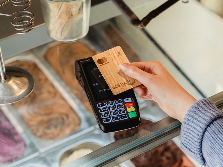 Eine Person bezahlt mit einer Holzbankkarte am Kartenlesegerät einer Eisdiele.