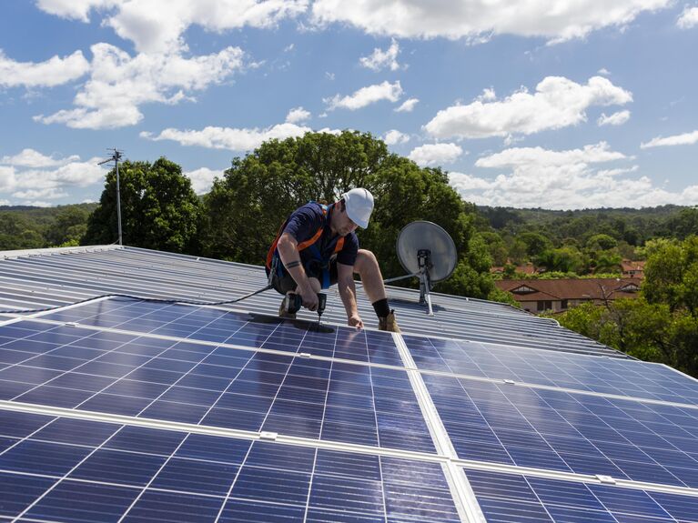 Männlich gelesene Person installiert eine Solaranlage auf dem dach.