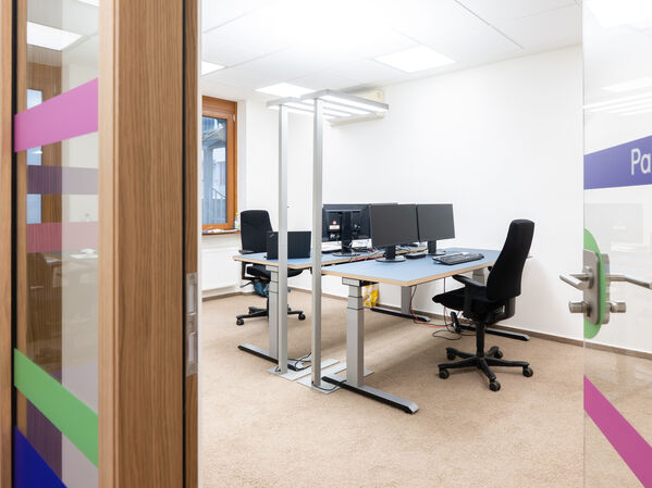 Ein Büroraum mit Schreibtisch, Monitor und Stuhl.