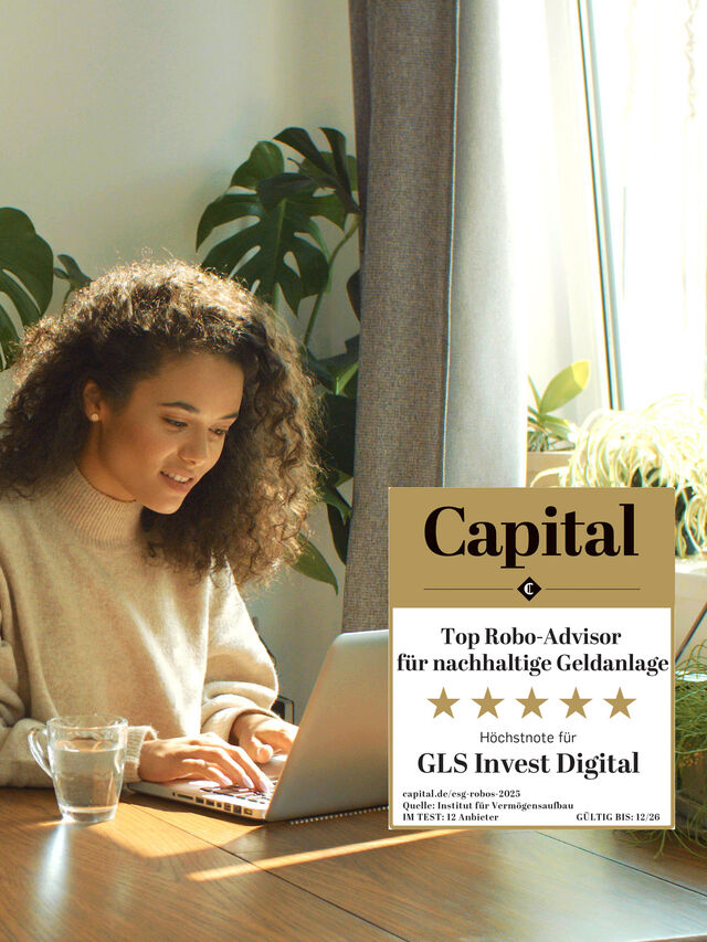 Frau arbeitet an einem Laptop an einem Holztisch in einer hellen, modernen Küche.