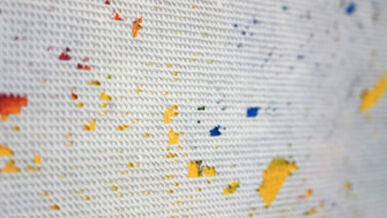 Nahaufnahme einer weißen strukturierten Oberfläche mit verstreuten farbigen Farbspritzern.