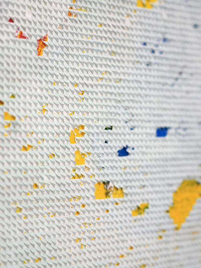 Nahaufnahme einer strukturierten weißen Oberfläche mit verstreuten gelben, blauen und roten Farbflecken.