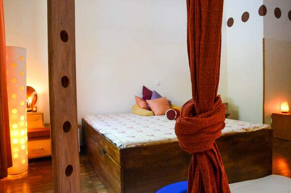 Ein gemütlich aussehendes Zimmer mit Holzbett und rotem Vorhang im Geburtshaus.