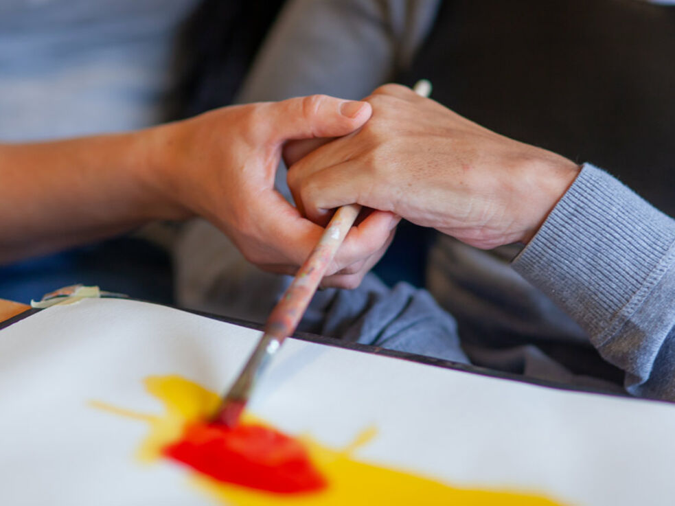 Eine Hand hilft einer anderen Hand beim Malen mit einem Pinsel