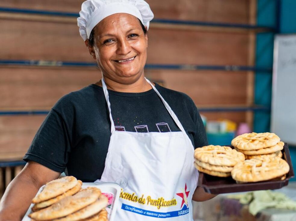 Daisy mit Schürze, Bäckermütze und zwei Tellern voller Gebäck