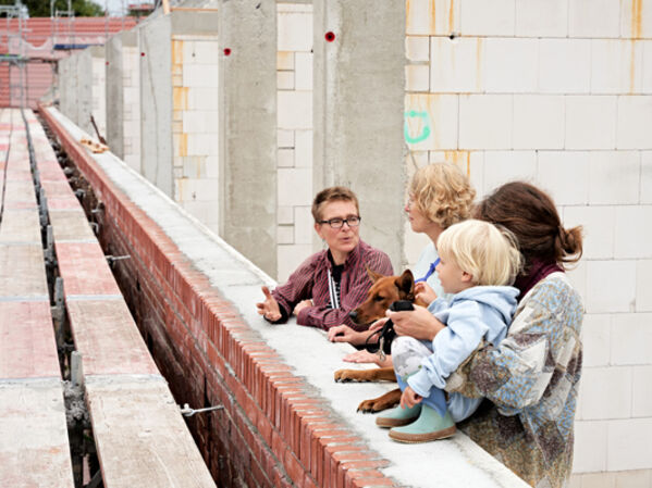 Drei weiblich gelesene Personen und ein Kind stehen an einer Mauer auf einer Baustelle.