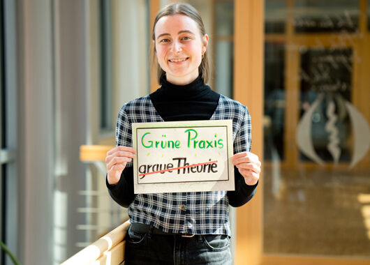 Mitarbeiterin der GLS Bank mit Plakat "Grüne Praxis statt grauer Theorie"