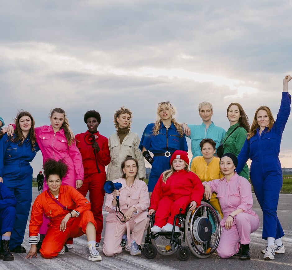 Eine Gruppe von weiblich gelesenen Personen in bunten Overalls.