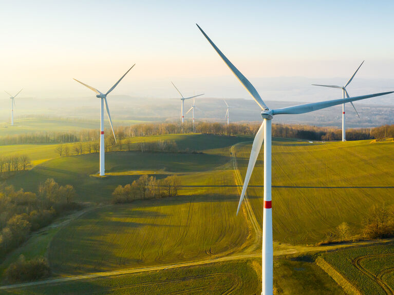 Windkraftanlagen stehen auf grasbewachsenen Hügeln unter einem klaren Himmel in einer ländlichen Landschaft.