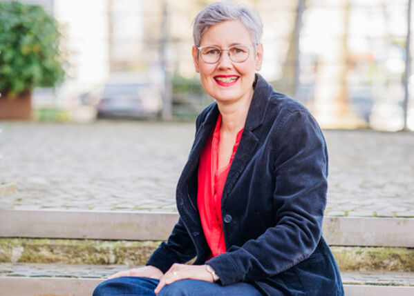 Antje Tönnis lächelnd auf einer Bank sitzend.