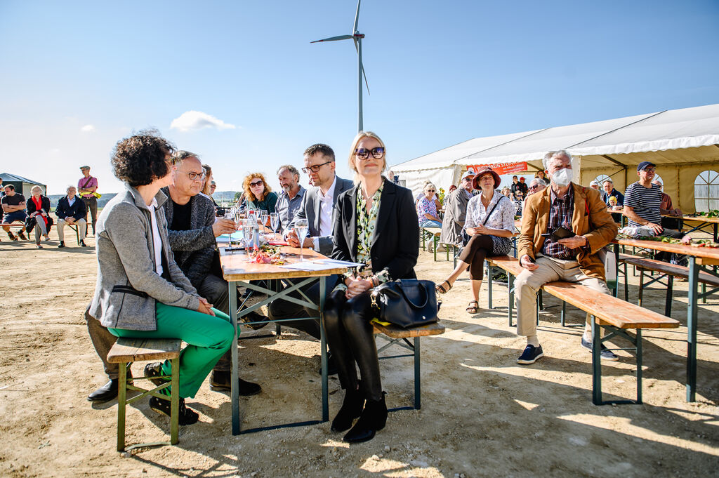 Menschen sitzen an einem sonnigen Tag bei der Einweihung der Windkraftanlage.