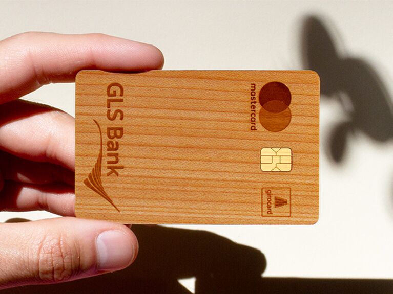 Holzkarte der GLS Bank vor weißer Wand, auf der Schatten einer Pflanze zu sehen sind