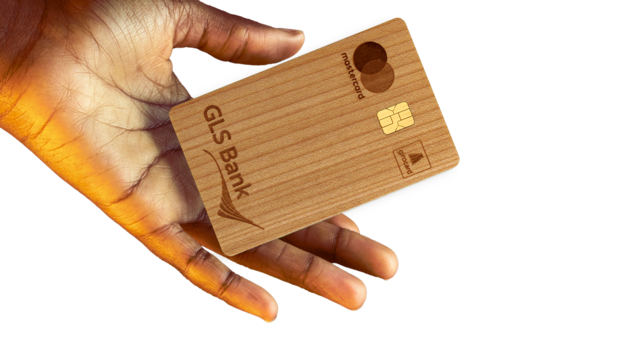 Eine Hand hält eine hölzerne GLS Bank Mastercard-Kreditkarte vor einem weißen Hintergrund.