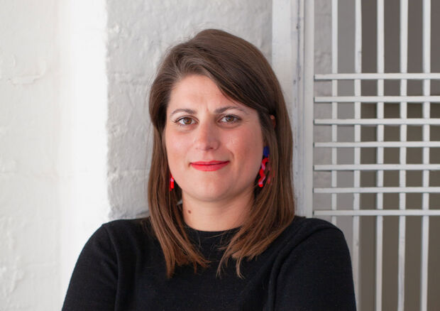 Weiblich gelesene Person mit glattem braunem Haar, rotem Lippenstift und schwarzem Oberteil steht in einem Haus.