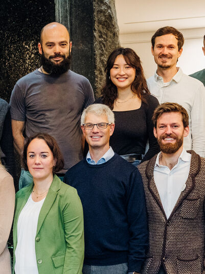 Eine Gruppe von 18 Personen, die in einem Haus zusammen stehen und für ein Foto posieren.