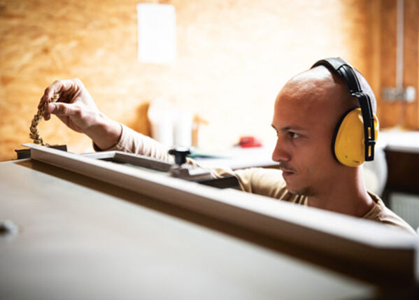 Männlich gelesene Person mit Ohrschützern in einer Werkstatt.