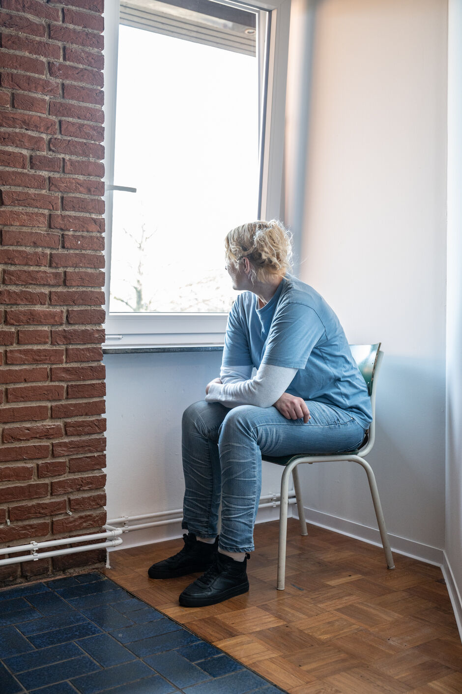 Eine weibliche gelesene Person sitzt am Fenster und schaut raus.